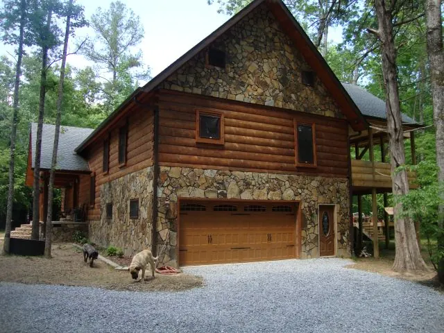 Cedar log home with a stone base among tall trees
